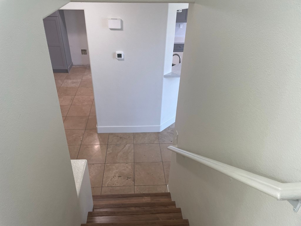 a look down the stairs of a home with a hallway and a laundry room