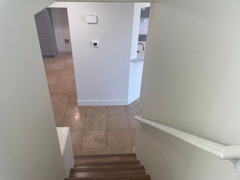 a look down the stairs of a home with a hallway and a laundry room