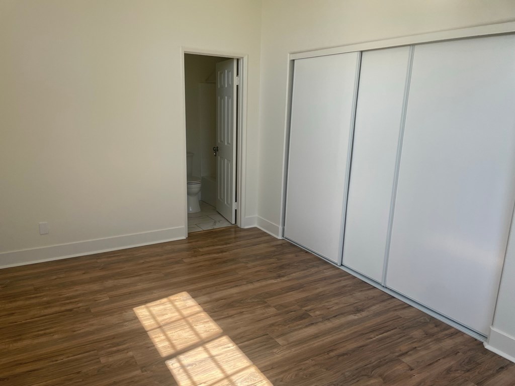 a bedroom with white walls and wood flooring and a closet