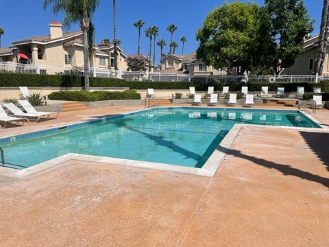 a swimming pool with chairs and trees and a building in the background