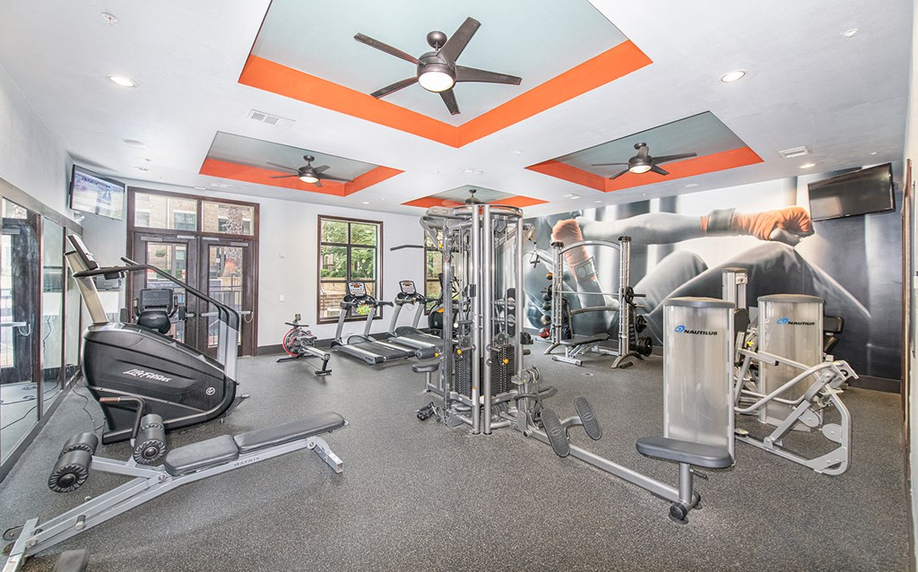 a gym with weights and cardio machines and a ceiling fan
