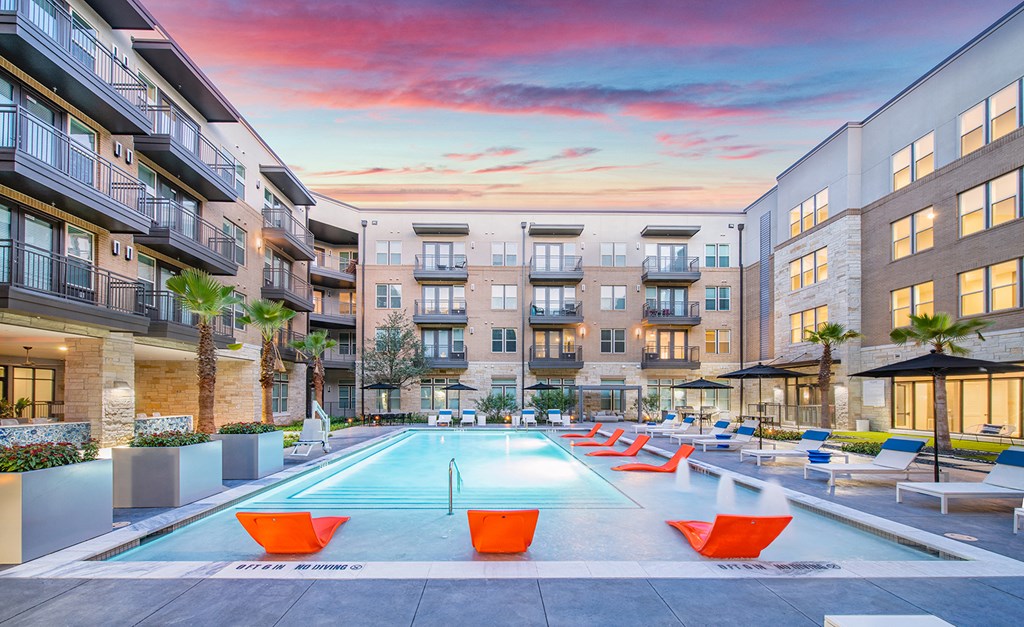 an apartment swimming pool with orange chairs in front of an apartment building