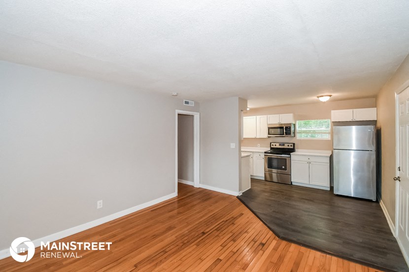 the living room and kitchen of an apartment with wood flooring and stainless steel appliances