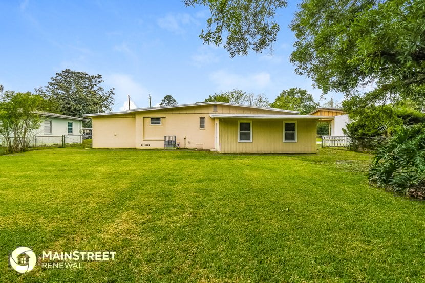 a beige house with a large grassy yard and trees