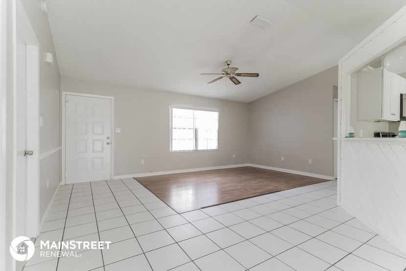 an empty living room with white tile and a ceiling fan