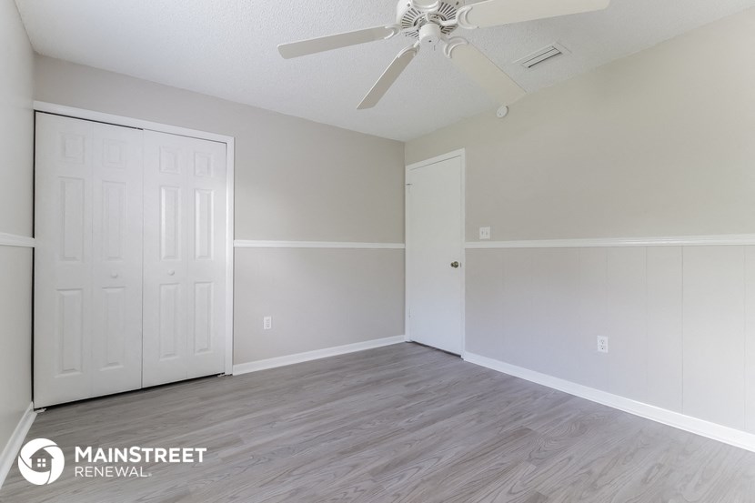 the spacious living room with white walls and a ceiling fan