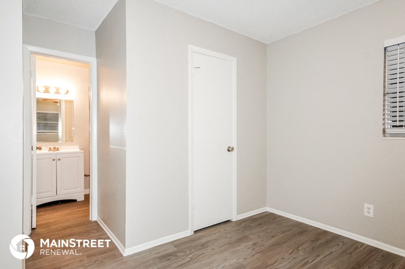 a bedroom with white walls and wood flooring and a door to the bathroom