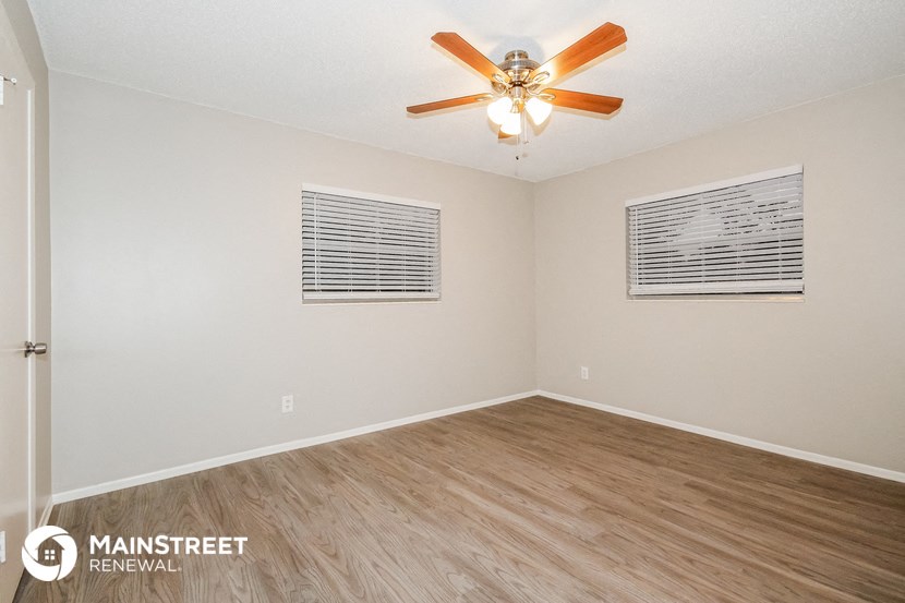 the spacious living room with wood flooring and ceiling fan