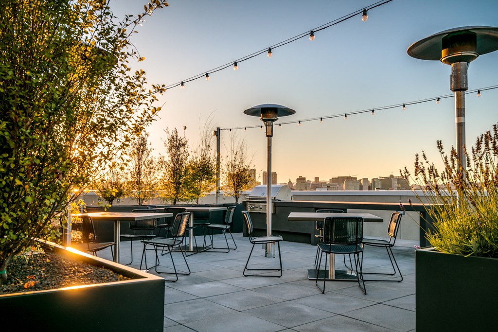 a rooftop patio with tables and chairs and a city skyline in the background