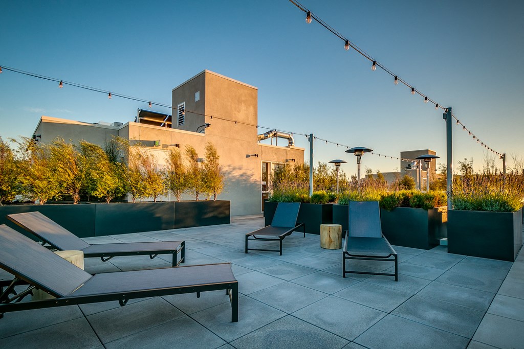 a rooftop patio with lounge chairs and tables and a building in the background