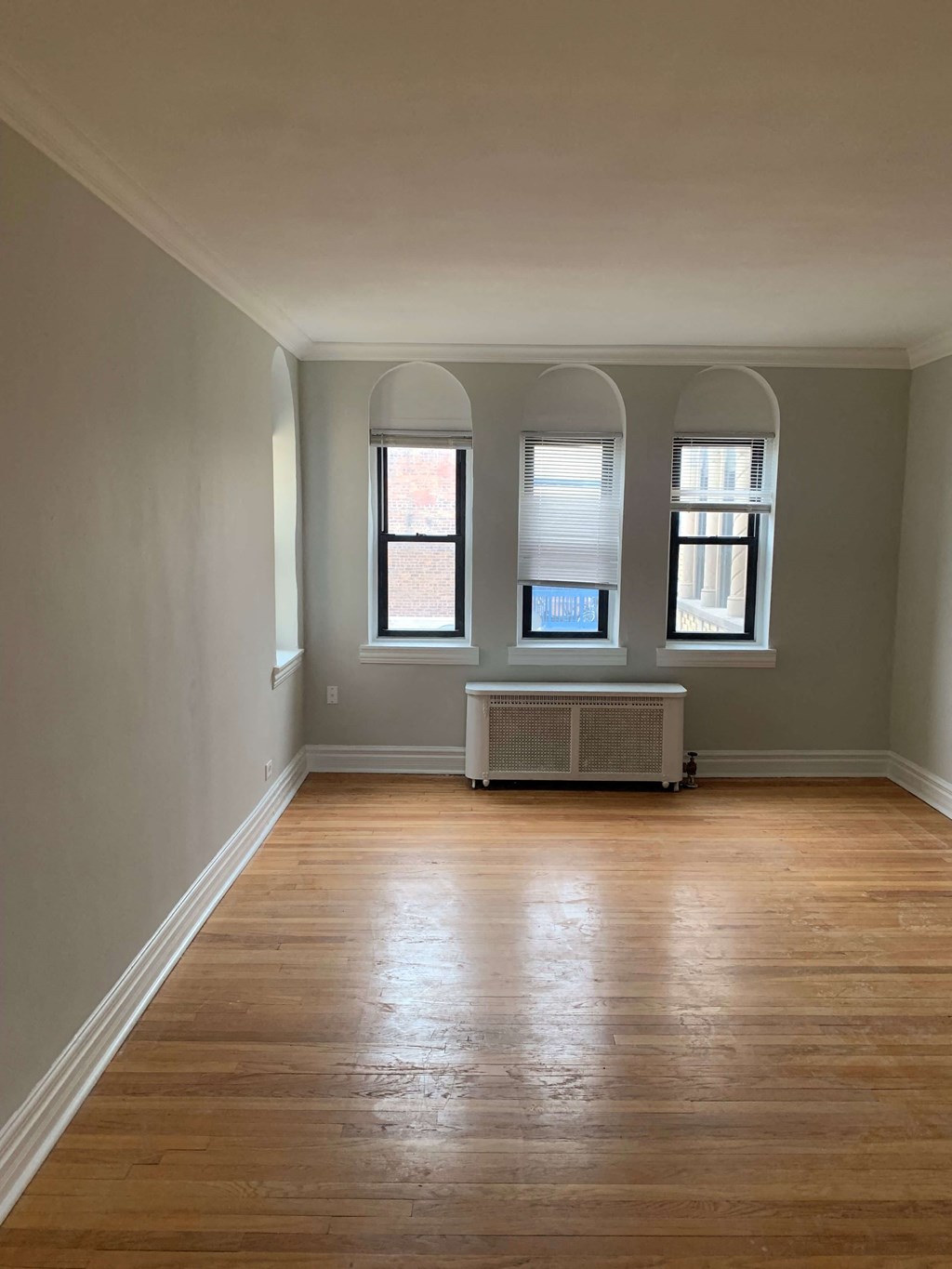 an empty living room with wooden floors and three windows