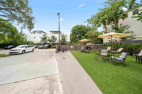 a patio with chairs and umbrellas on a lawn next to a sidewalk