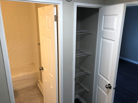 a walk in closet in a bathroom with a door open to a shower and tub