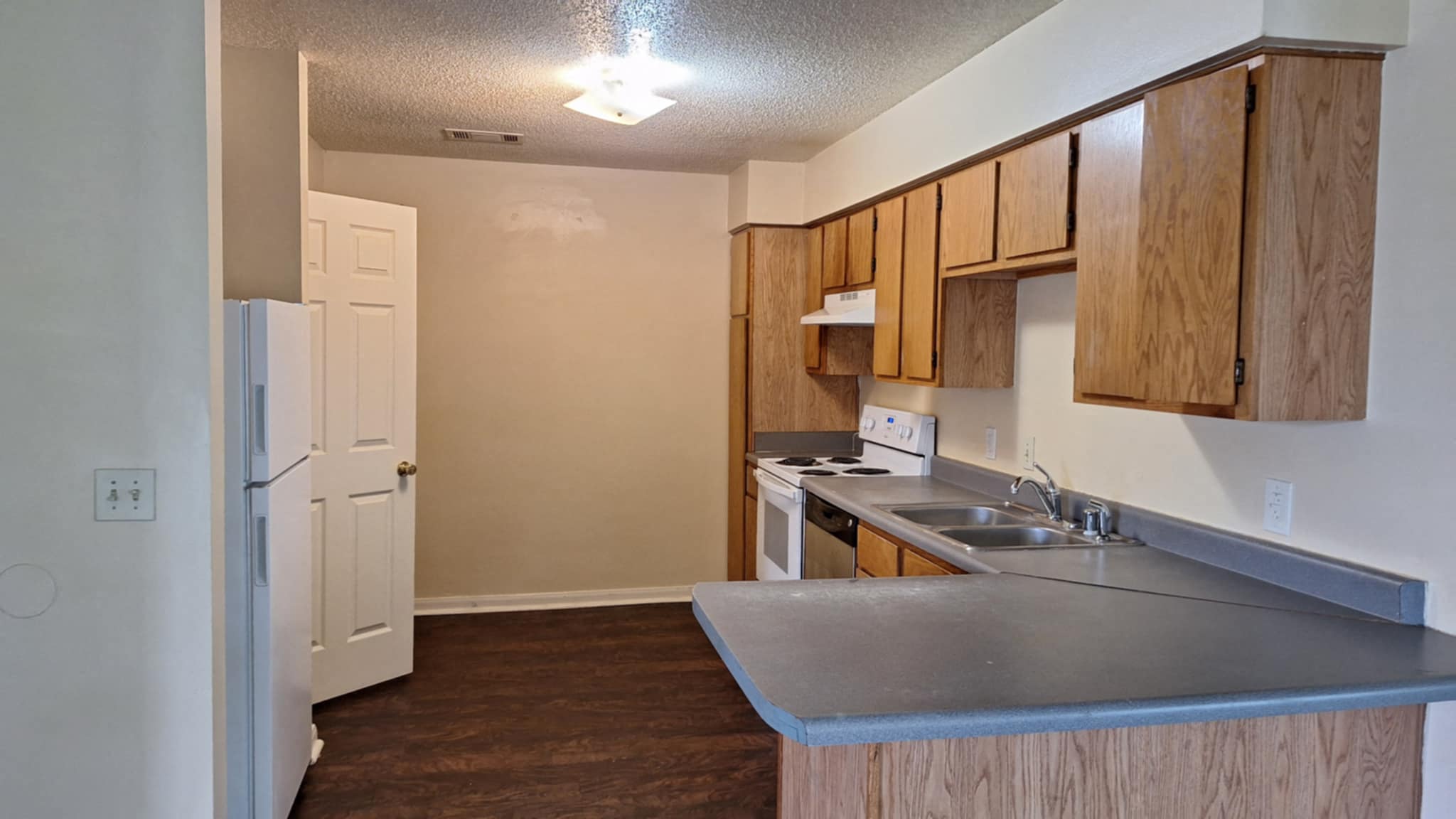 A kitchen with a white refrigerator, wooden cabinets, and a stainless steel counter.