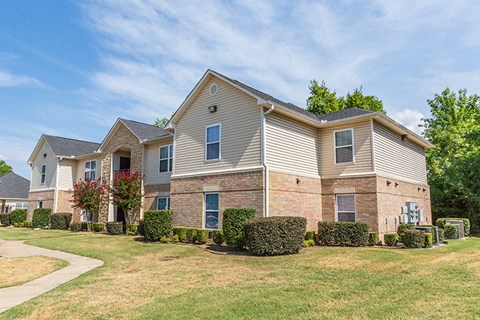 an apartment building with brick and tan siding and trees