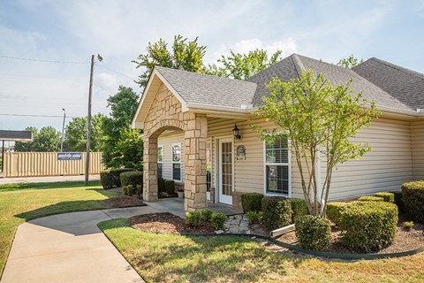 a small tan house with a driveway and a tree in front of it
