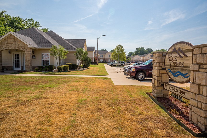 a sign in front of a house with cars parked in a driveway