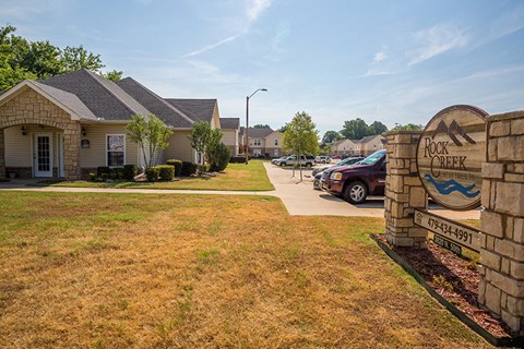 a sign in front of a house with cars parked in a driveway