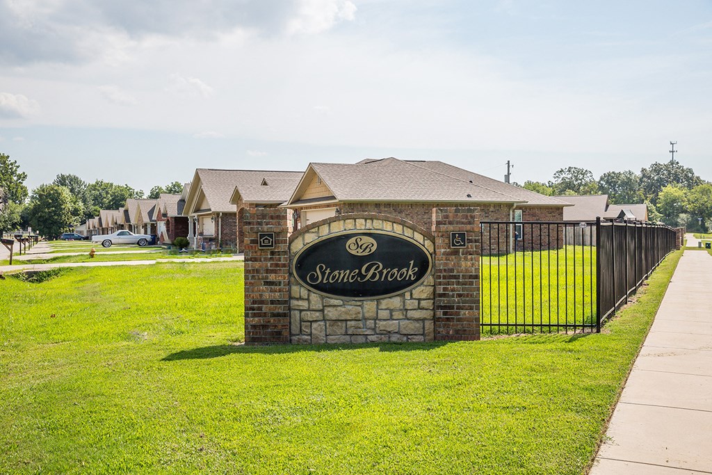 a stone building with a fence and a sign for stonebrook apartments