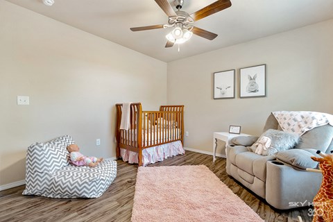the master bedroom has a crib and a couch and a ceiling fan