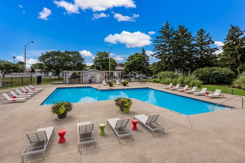 A pool surrounded by lawn chairs and trees.