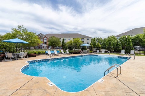 A large outdoor swimming pool surrounded by a fence and lounge chairs.