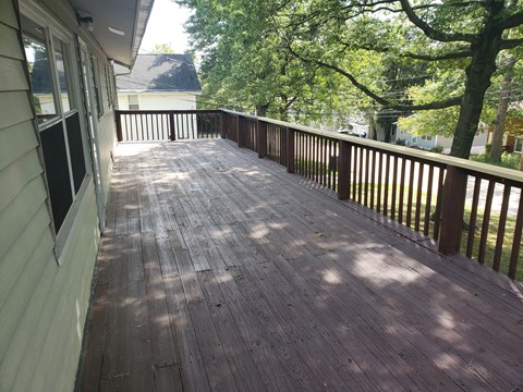 A wooden deck with a railing and trees in the background.