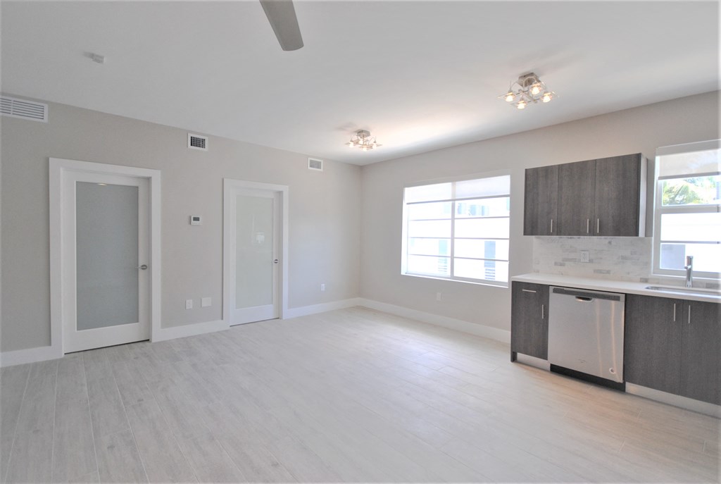 an empty living room with a kitchen and a window