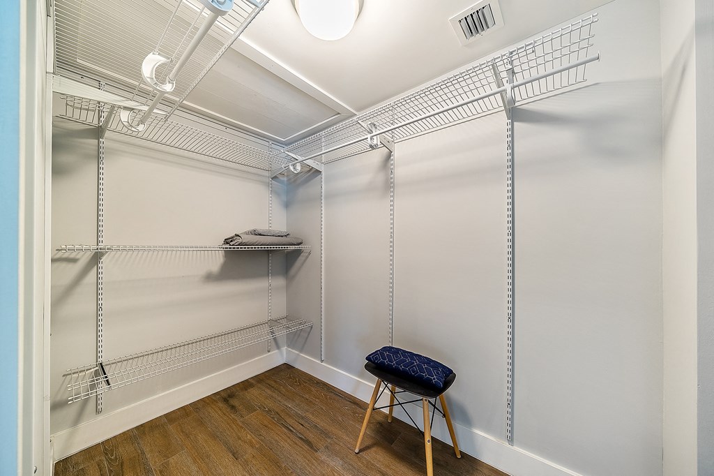 a walk in closet with wire shelving and a stool