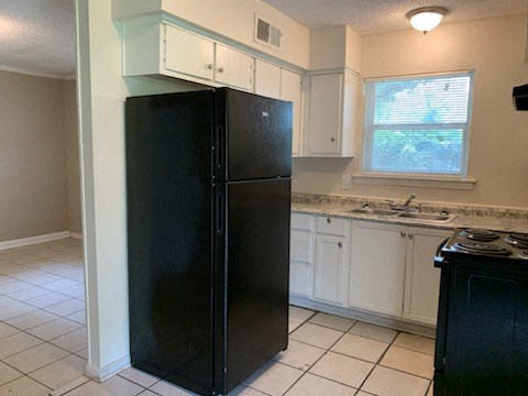 A black refrigerator in a kitchen with white cabinets.