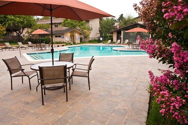 a swimming pool with a patio with tables and chairs