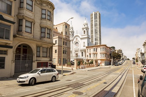 A silver car is parked on the side of a street with tram tracks.