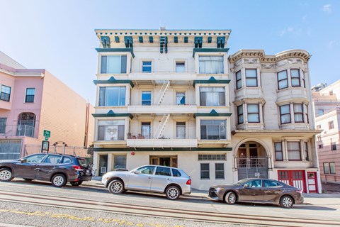 A row of three-story buildings with cars parked in front.