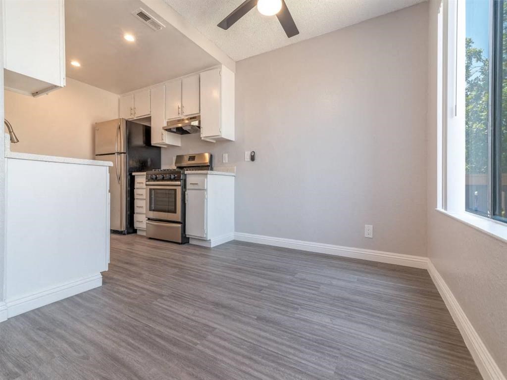 an empty living room with a kitchen and a ceiling fan