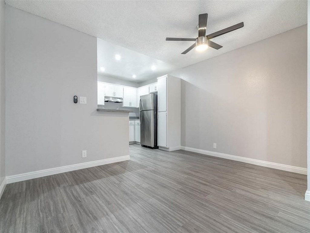 an empty living room with a refrigerator and a ceiling fan