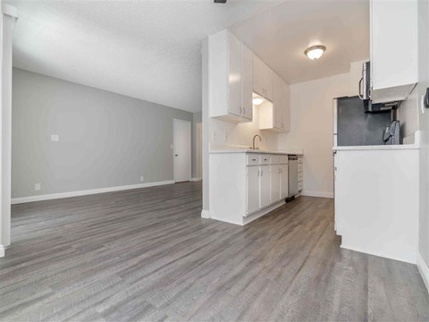 an empty living room and kitchen with white cabinets and a counter top
