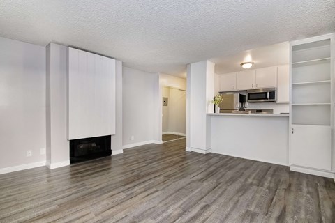 an empty living room with a fireplace and a kitchen