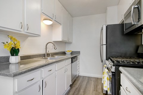 an apartment kitchen with white cabinets and stainless steel appliances