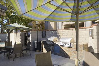 a patio with an outdoor grill and tables with umbrellas