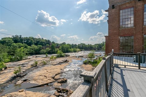 A view of a rocky river from a deck with a building in the background.