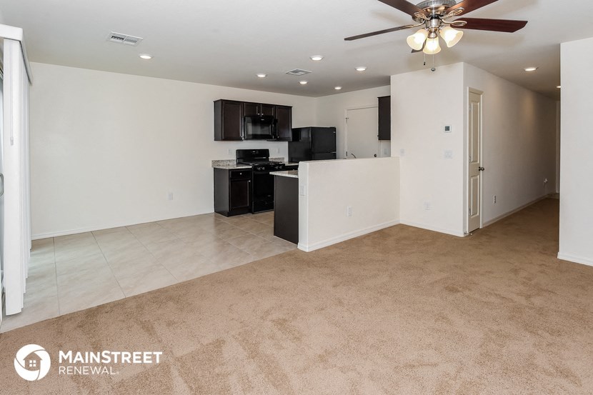 an empty living room with a kitchen and a ceiling fan