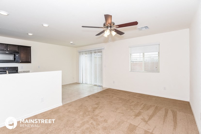 the living room and kitchen of a white house with a ceiling fan