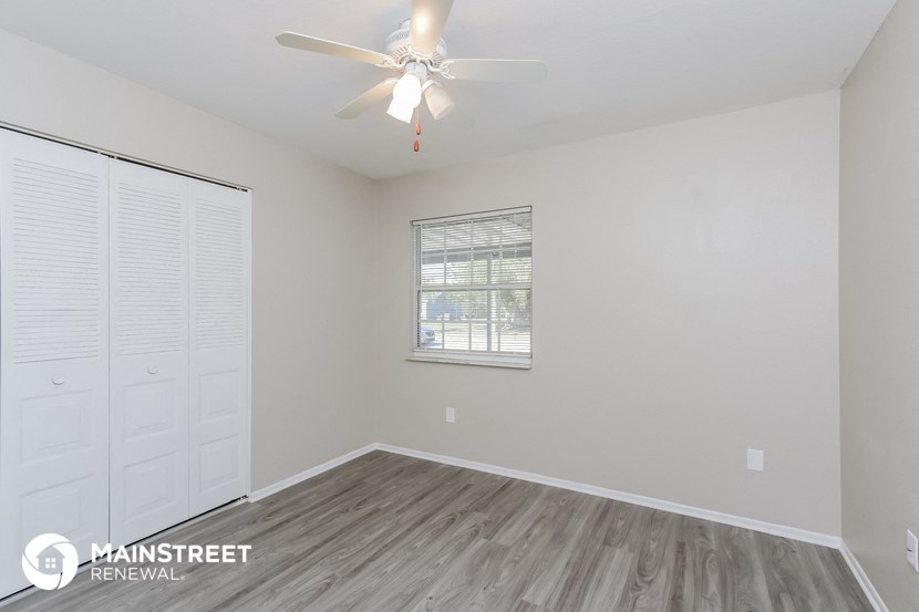 the living room of an apartment with white walls and a ceiling fan