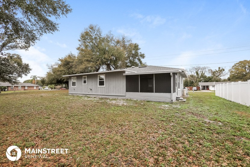 a small gray house with a yard and a white fence
