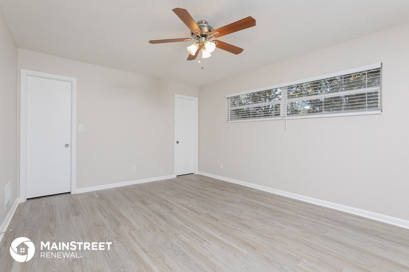 the living room of an apartment with white walls and a ceiling fan