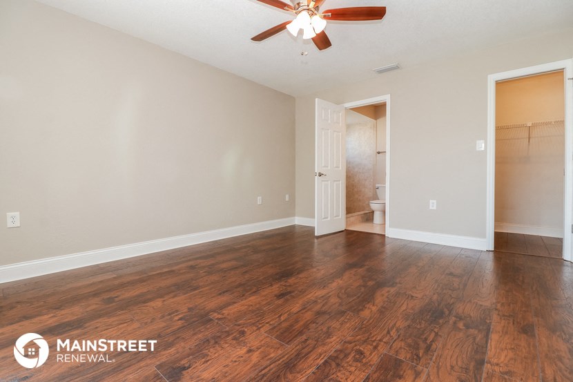 the spacious living room with hardwood flooring and a ceiling fan