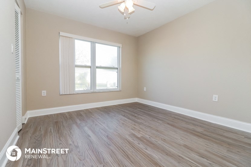 the spacious living room with wood flooring and a ceiling fan