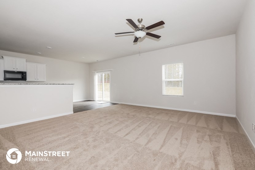 the living room and kitchen of an empty house with a ceiling fan