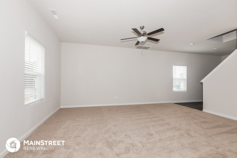 the spacious living room with ceiling fan and carpeting