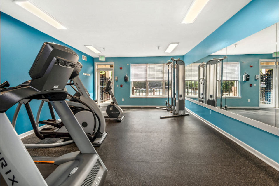 Fitness room with blue walls and a black floor. Exercise machines are lined up against the wall across from a wall-length mirror on the other wall.